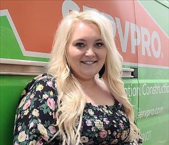 Blonde lady with flowered shirt in front of green van