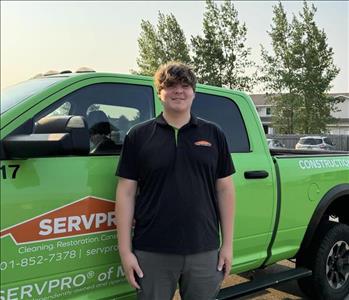 Man with brown hair and black polo shirt in front of green pickup